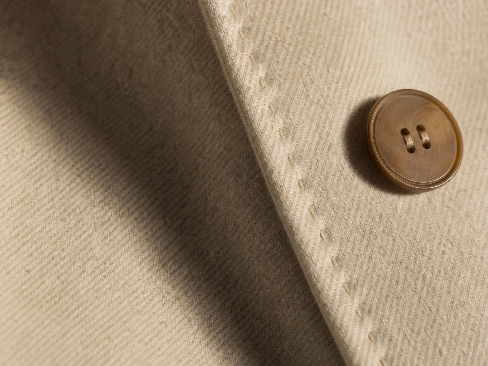 Macro photograph of cream double-face wool weave with a single horn button and pick-stitched seam